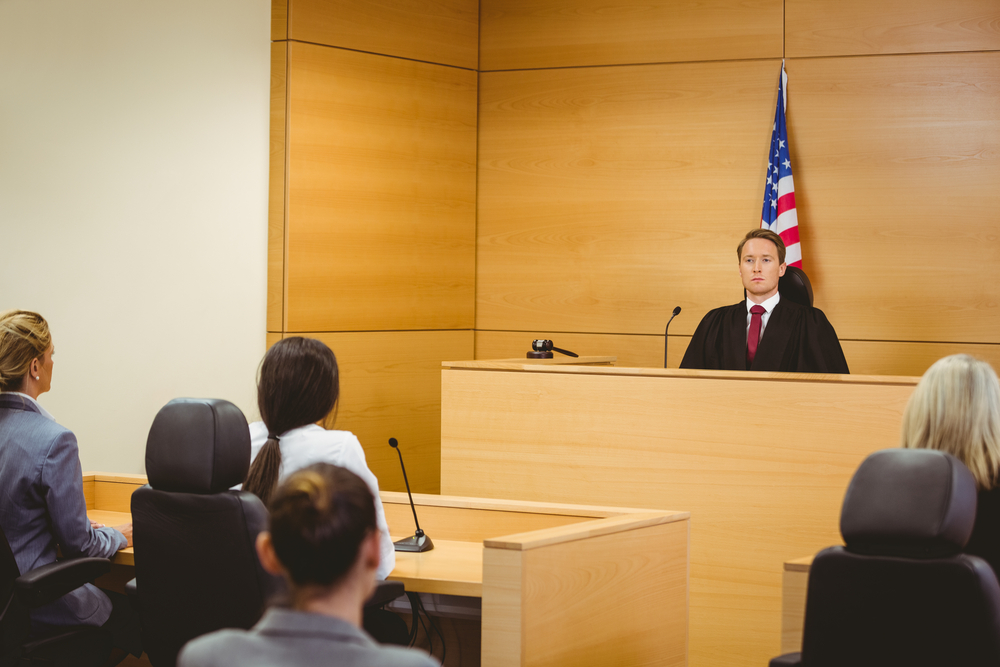 Unsmiling judge with american flag behind him in the court room